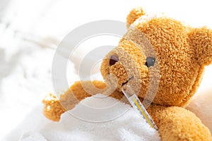 Teddy bear lying sick in hospital bed with with thermometer