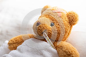 Teddy bear lying sick in hospital bed with with thermometer