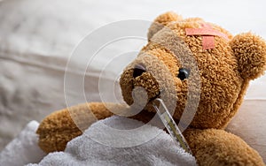 Teddy bear lying sick in hospital bed with with thermometer and plaster. Healthcare and medical concept