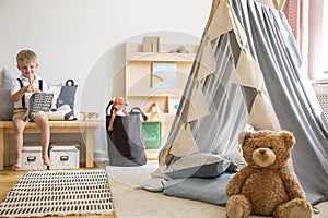 Teddy bear next to grey scandinavian tent in stylish boy`s bedroom with furniture made from natural materials, real photo with
