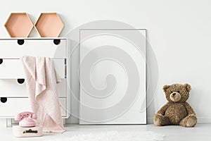 Teddy bear next to white empty poster in baby`s room interior wi