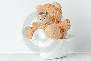 A teddy bear in a potty next to stack of diapers