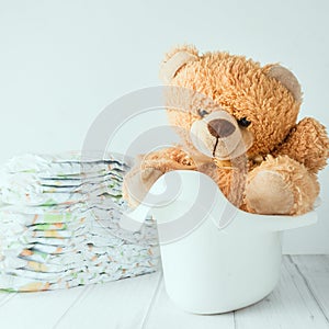 A teddy bear in a potty next to stack of diapers