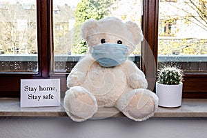 Teddy bear with protective medical mask in quarantine near the window. Stay home concept