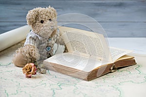Teddy bear reading antique book on the old map
