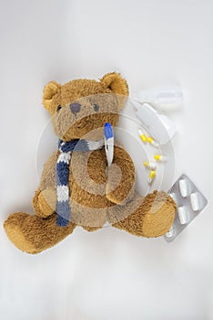 Teddy bear in a scarf with a thermometer and medicine on a light background