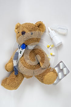 Teddy bear in a scarf with a thermometer and medicine on a light background