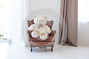 Teddy bear sits on an armchair in the apartment room near the window, children's toy in the bedroom, apartment