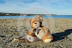 Teddy bear sitting alone on the sand on the beach - abandoned, depresion, violence or child abuse concept