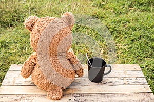 Teddy bear sitting backwards and coffee cup on wooden table.