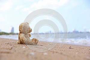 Teddy bear sitting on the beach look on the sea feel lonely.