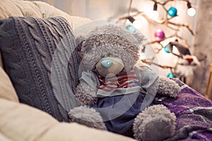 Teddy bear sitting on chair with gray pillow.