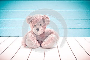 Teddy bear sitting on white wooden floor with blue-green background lonely