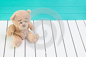 Teddy bear sitting on white wooden floor with blue-green background lonely