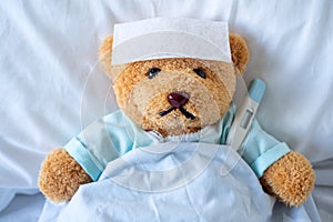 The teddy bear slept with a high fever in the bed. Together with a thermometer