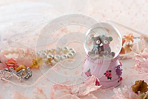 Teddy bear in snow globe decoration on pink fabric background.