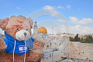 Teddy bear on a sunny day on the background of the Golden Dome and the Wailing Wall in Jerusalem. Toy with the flag of Israel