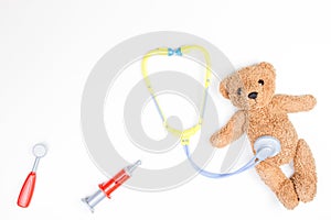 Teddy bear with toy stethoscope and toy medicine tools on a white background.