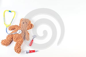 Teddy bear with toy stethoscope and toy medicine tools on a white background. Top view