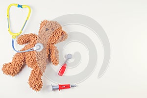 Teddy bear with toy stethoscope and toy medicine tools on a white background. Top view