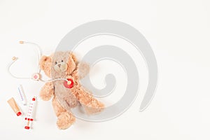 Teddy bear with toy stethoscope and wooden toy medicine tools on a white background. Top view. Concept of children's