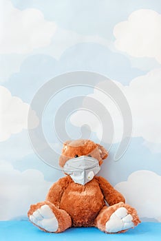 Teddy bear wearing flu mask sits on blue sky background. Sick concept, or environmental pollution, gas pollution