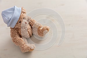 Teddy bear wearing pastel blue cap on wooden background, copy space