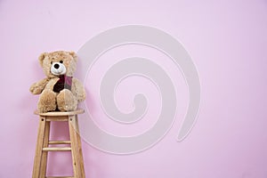 Teddy Bear on a wooden chair pink walls.