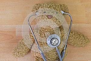 Teddy bear on wooden floor with stethoscope with earpieces in ea
