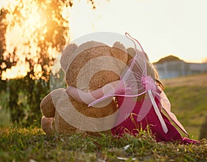 Teddy is her best friend. Rearview shot of a cute little girl playing with a huge teddybear in the park.