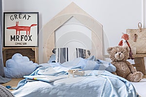 Teddy next to blue bed with sheets in kid`s bedroom interior with fox poster. Real photo