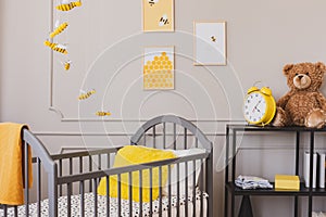 Teddy and yellow clock on industrial metal shelf in cute baby bedroom