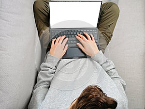 Teeanger sitting on the sofa with laptop. Top view of laptop mokup. home schooling, online game playing, media