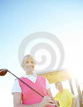 Teeing off at tea time. Low angle shot of an attractive older female golfer standing in front of a golf cart with her