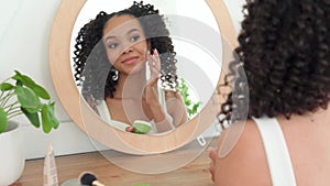 Teen African American girl sitting looking at mirror applying facial cream.