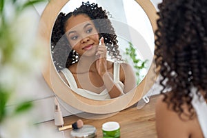 Teen African girl looking in bathroom mirror applying facial cream on face.