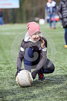 Teen age girl football player holding ball with hands while sitting on an artificial green field