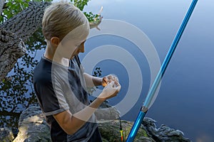 The teen angler checks the bait and puts a new one on. Sport fishing on the river in summer