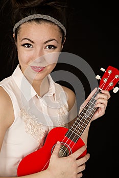 Teen Asian American girl playing a red ukulele