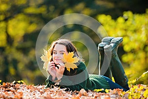 Teen in the autumn park. Smiling young girl lying on autumn maple leaves at fall outdoors. Portrait of a beautiful