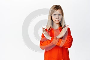 Teen blond girl showing cross, stop rejection gesture, prohibit smth, disagree, showing taboo block, standing over white