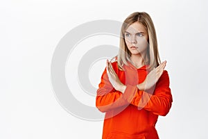 Teen blond girl showing cross, stop rejection gesture, prohibit smth, disagree, showing taboo block, standing over white