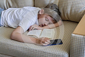 Teen blonde boy sleeping with an open book and a phone.