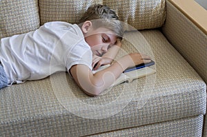 Teen blonde boy sleeping with an open book and a phone.