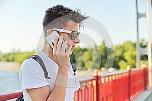 Teen boy 15, 16 years old with sunglasses fashionable haircut talking on smartphone