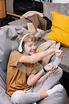 Teen boy actively and recklessly playing video game with joystick sitting on frameless beanbag chair