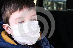 A teen boy in car wearing white surgical medical face mask as a protection against virus disease