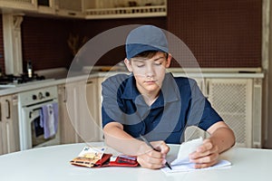 Teen boy is counting checking the pocket money in his wallet, home background. Freelancer, work for students, first