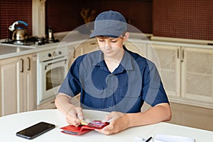 Teen boy is counting checking the pocket money in his wallet, home background. Freelancer, work for students, first