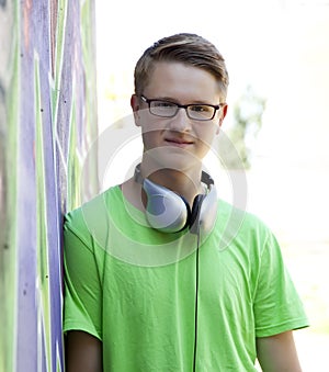 Teen boy with earphones near graffiti wall.